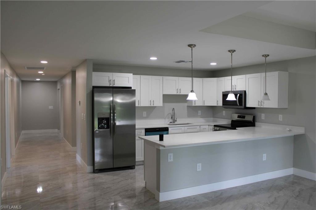 Kitchen with appliances with stainless steel finishes, sink, kitchen peninsula, white cabinetry, and decorative light fixtures