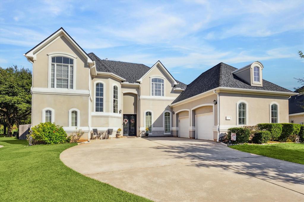 This home features a modern design with a light exterior, large windows, and a spacious two-car garage. The front yard is well-maintained, with a curved driveway and lush greenery, creating an inviting entrance.