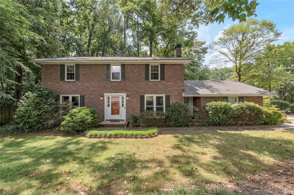 a view of a brick house next to a yard with plants and trees