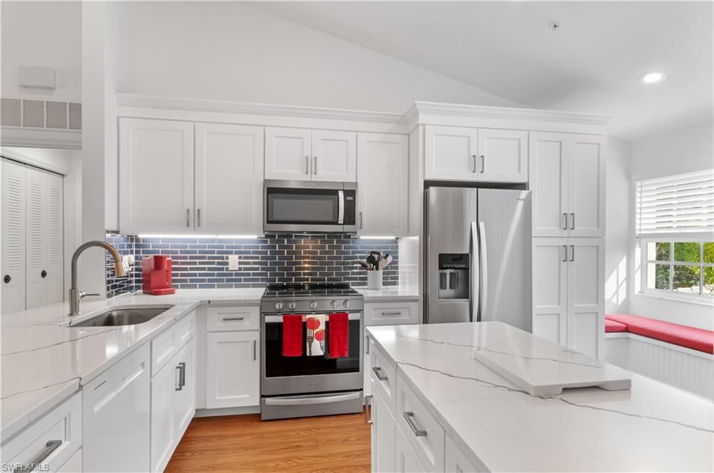 Kitchen with vaulted ceiling, light hardwood / wood-style flooring, stainless steel appliances, light stone countertops, and sink