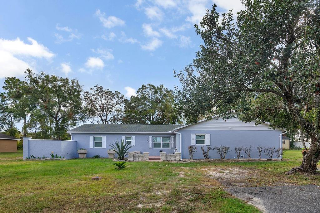 a house that is sitting in the grass with large trees and plants