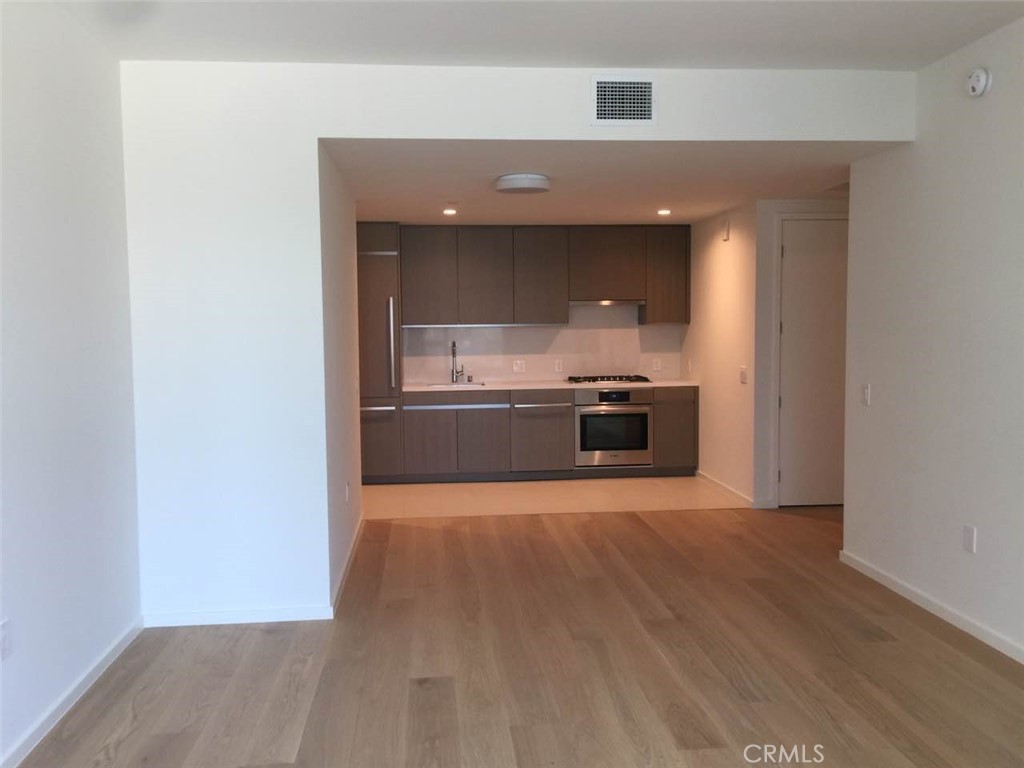 an empty room with wooden floor and a kitchen