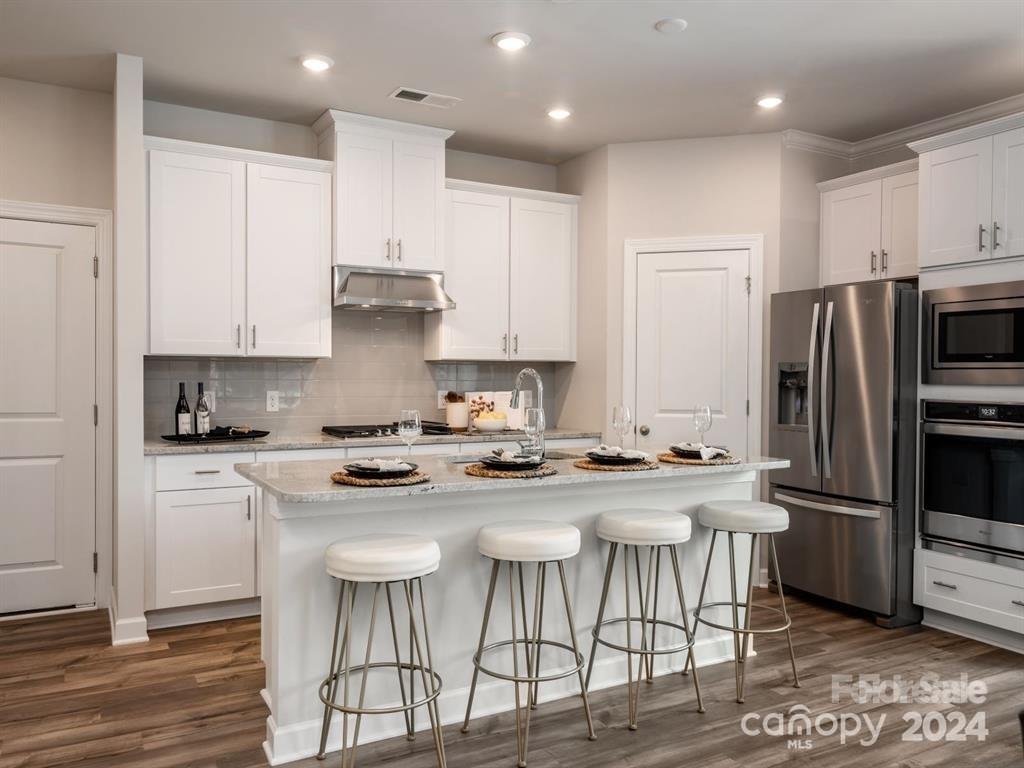 a kitchen with stainless steel appliances granite countertop a stove a sink a refrigerator and white cabinets with wooden floor