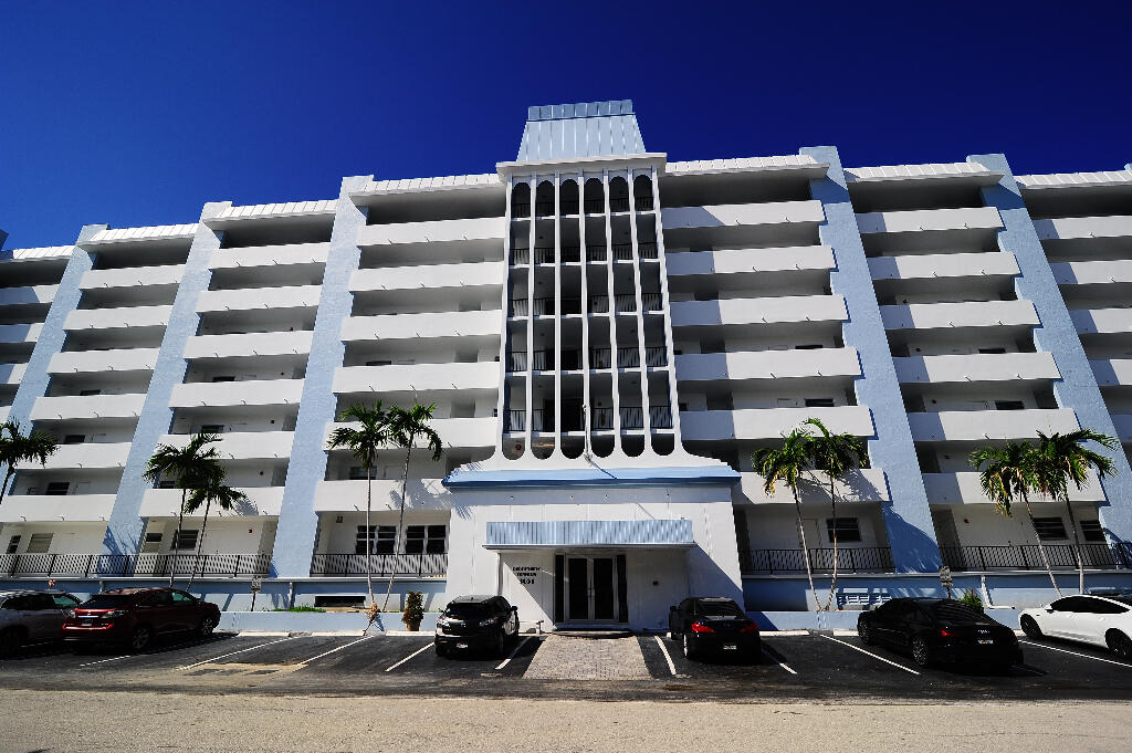 a front view of a building with lot of cars and trees