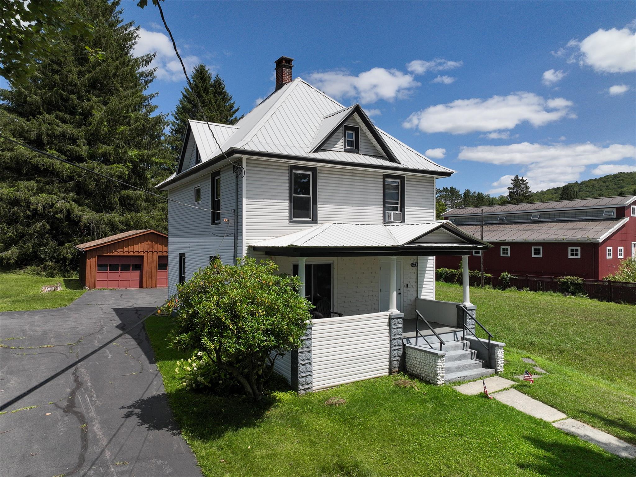 View of front of property with covered porch, a garage, a front lawn, and an outdoor structure