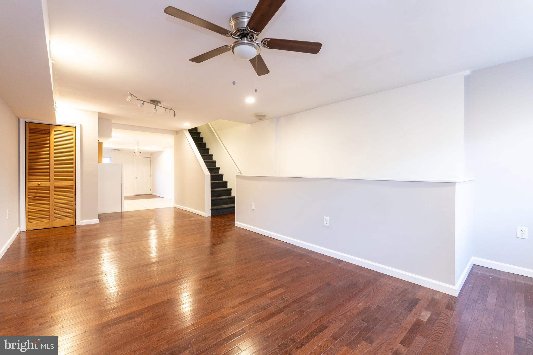 a view of an empty room with wooden floor and a ceiling fan