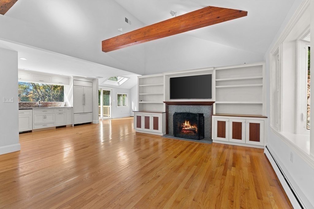 a view of an empty room with wooden floor fireplace and a window