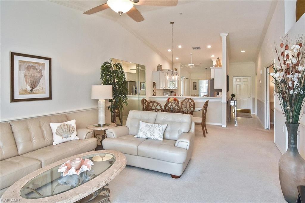 Living room with ceiling fan, ornamental molding, light carpet, and high vaulted ceiling