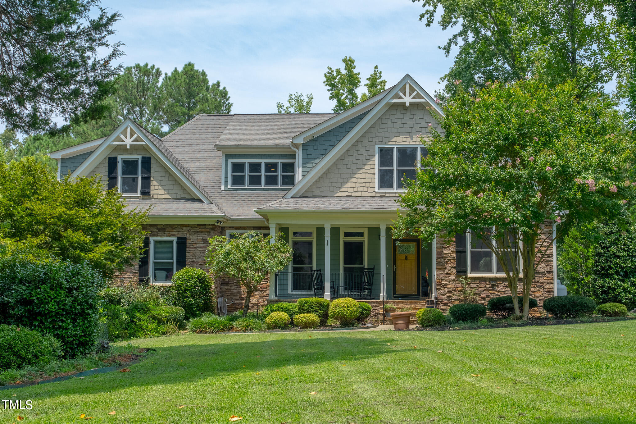 a house that is sitting in front of a big yard with potted plants and large trees