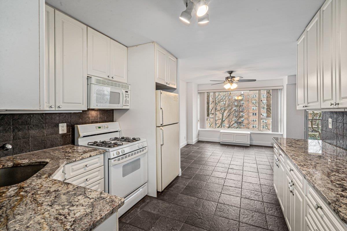 Kitchen with sink, white cabinetry, white appliances, ceiling fan, and stone countertops