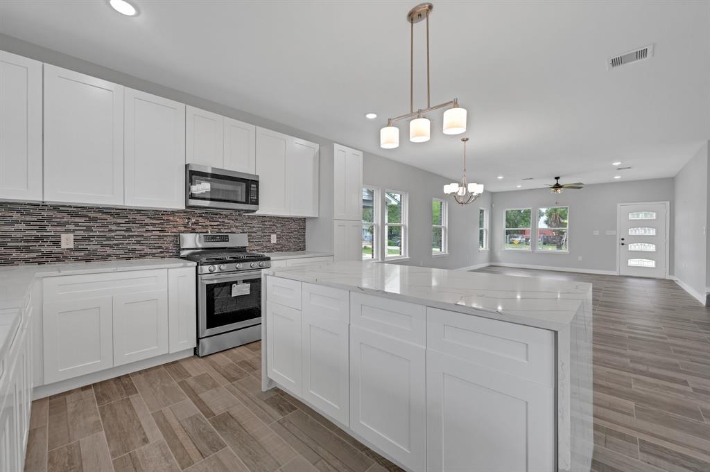 a kitchen with stainless steel appliances kitchen island granite countertop a stove a sink and a white cabinets