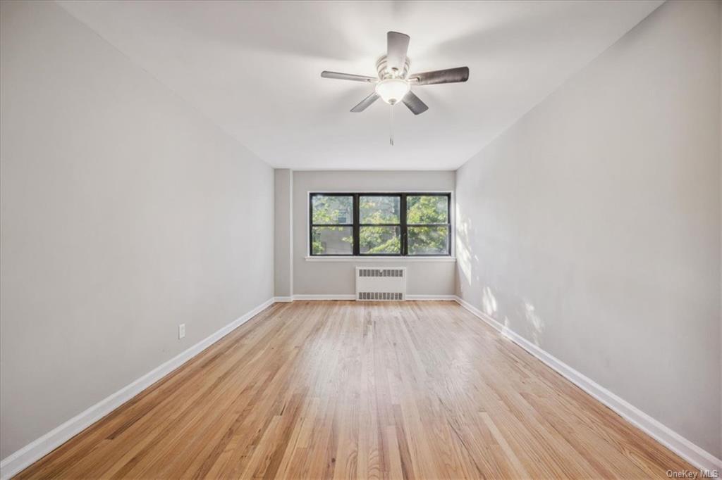 Empty room featuring light hardwood / wood-style floors, radiator heating unit, and ceiling fan