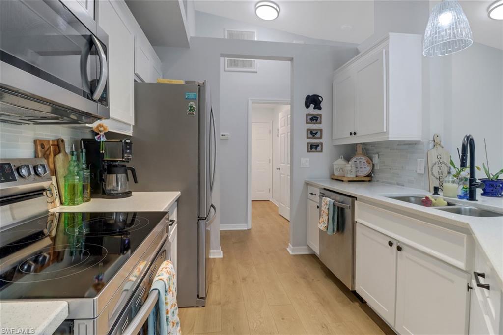 Kitchen featuring backsplash, stainless steel appliances, light hardwood / wood-style flooring, white cabinetry, and lofted ceiling