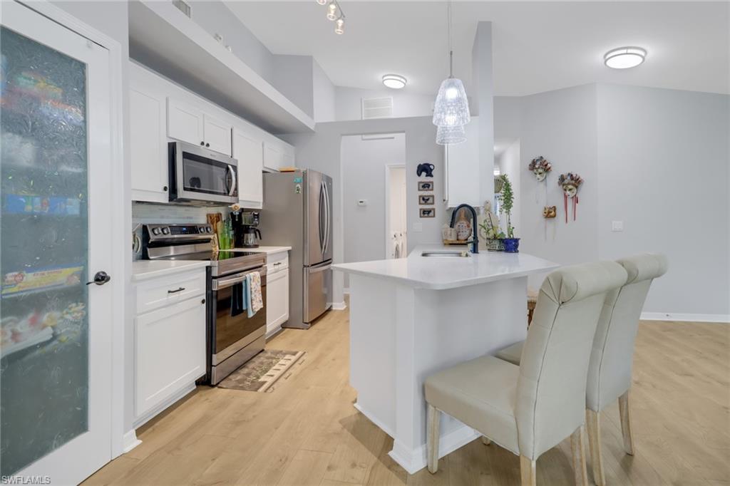 Kitchen with light wood-type flooring, backsplash, pendant lighting, white cabinetry, and appliances with stainless steel finishes