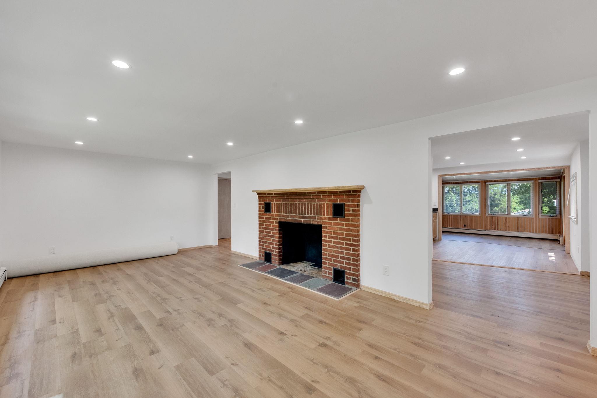 a view of an empty room with wooden floor fireplace and a window