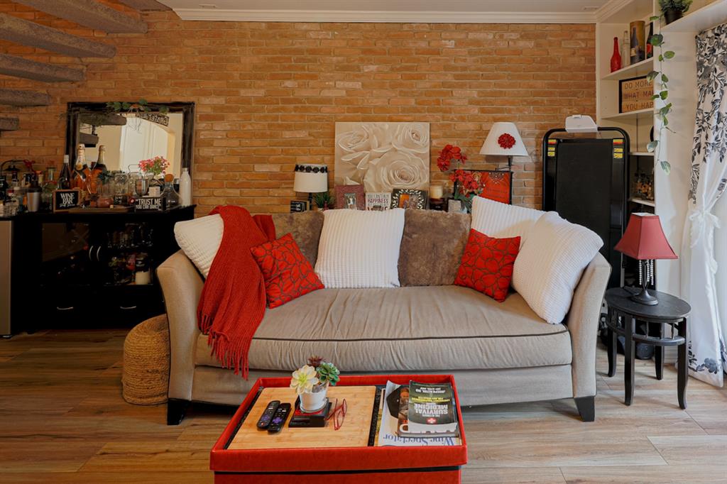 This cozy living space features warm brick walls. Natural light, built-in shelves and wooden flooring add to the inviting ambiance.