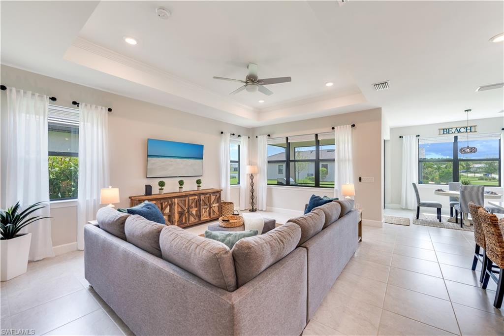 Tiled living room with a wealth of natural light, ceiling fan, and a raised ceiling