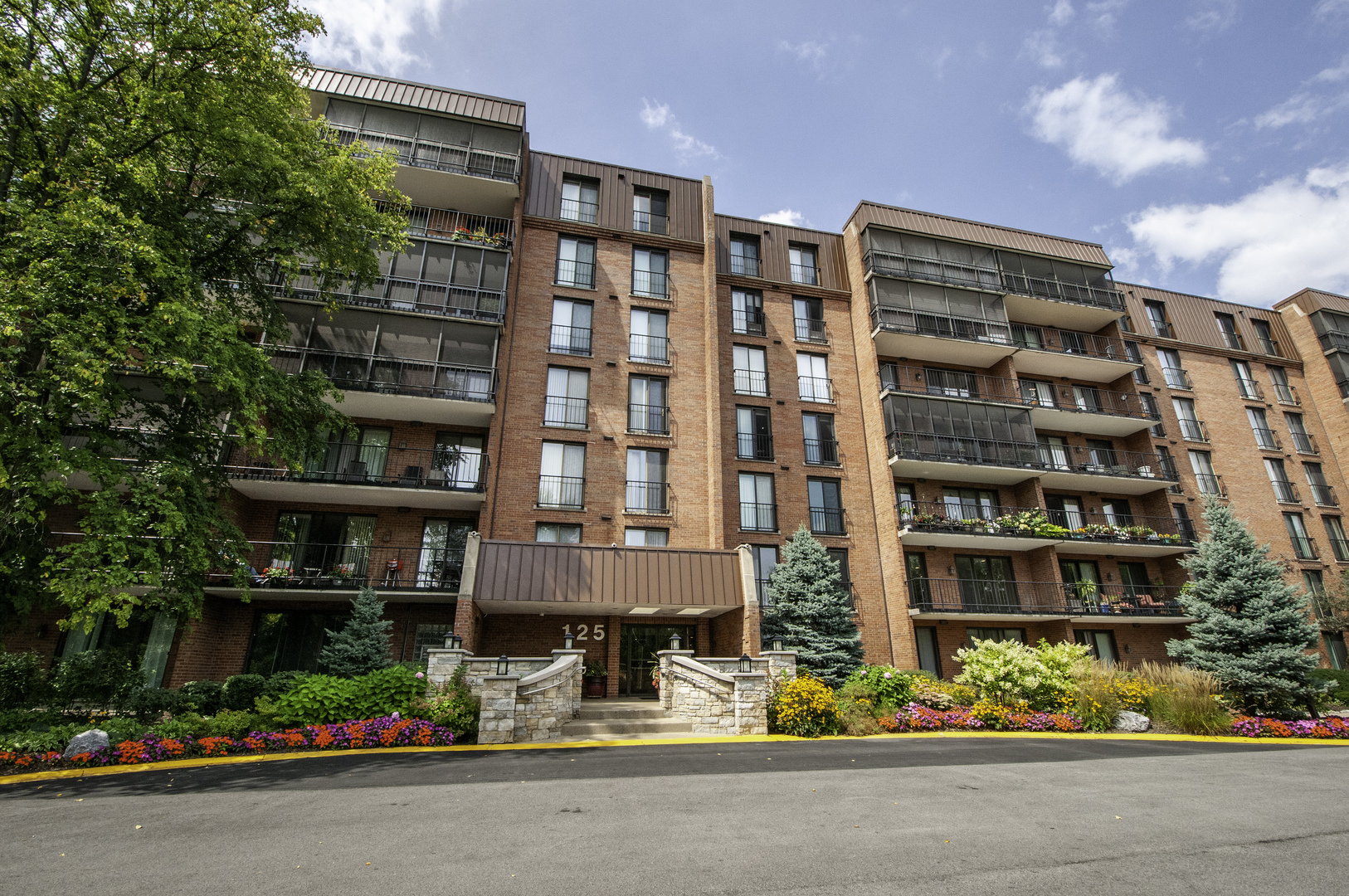 a front view of a multi story residential apartment building with yard and parking