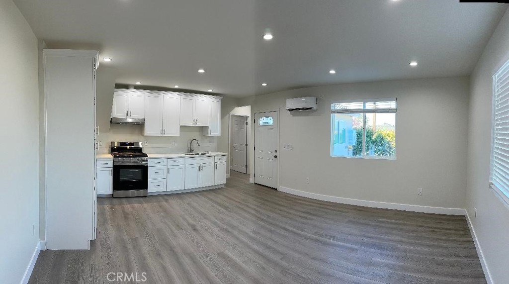 a view of kitchen with kitchen island granite countertop a refrigerator oven a sink and white cabinets with wooden floor