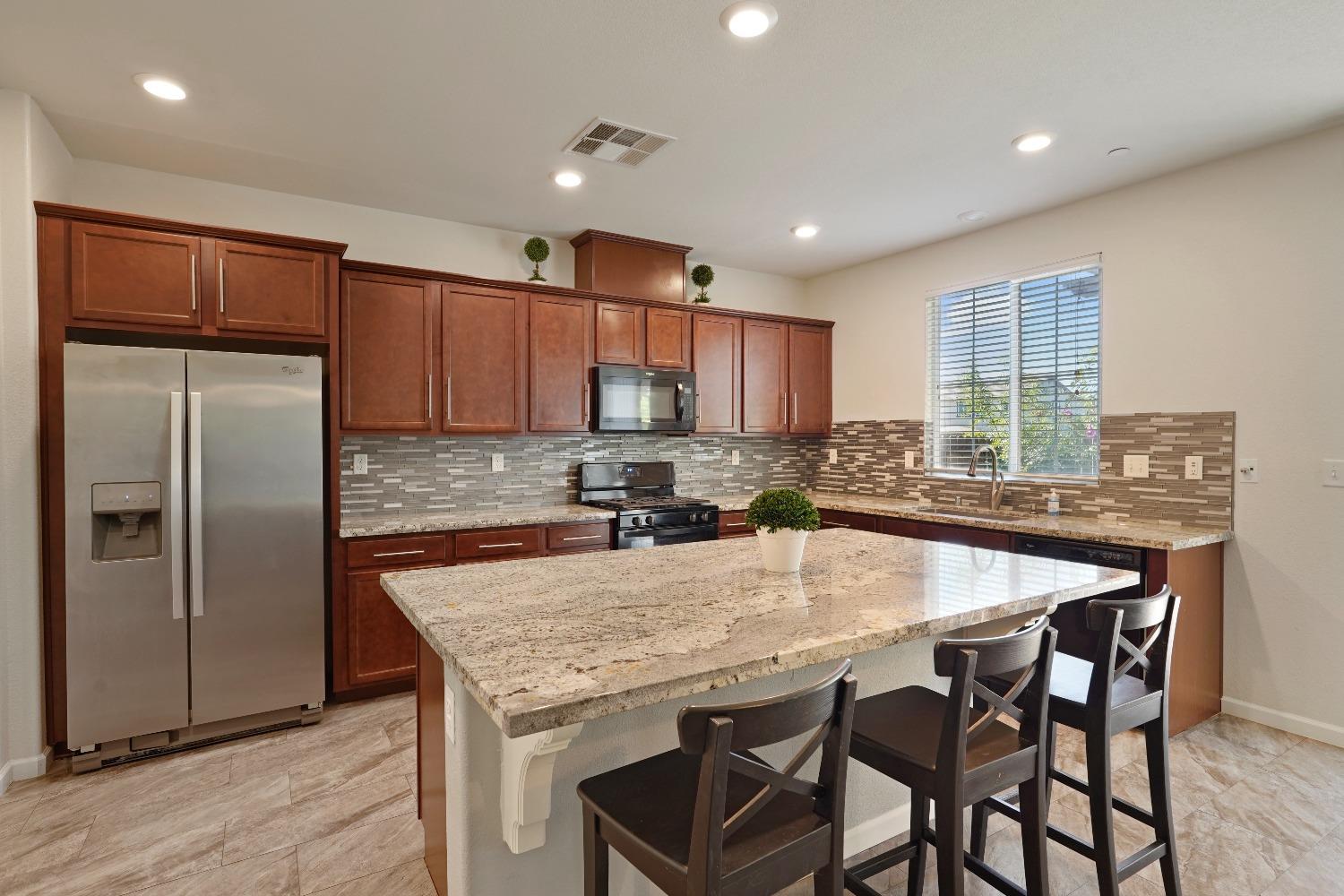 a kitchen with granite countertop a table chairs microwave and refrigerator