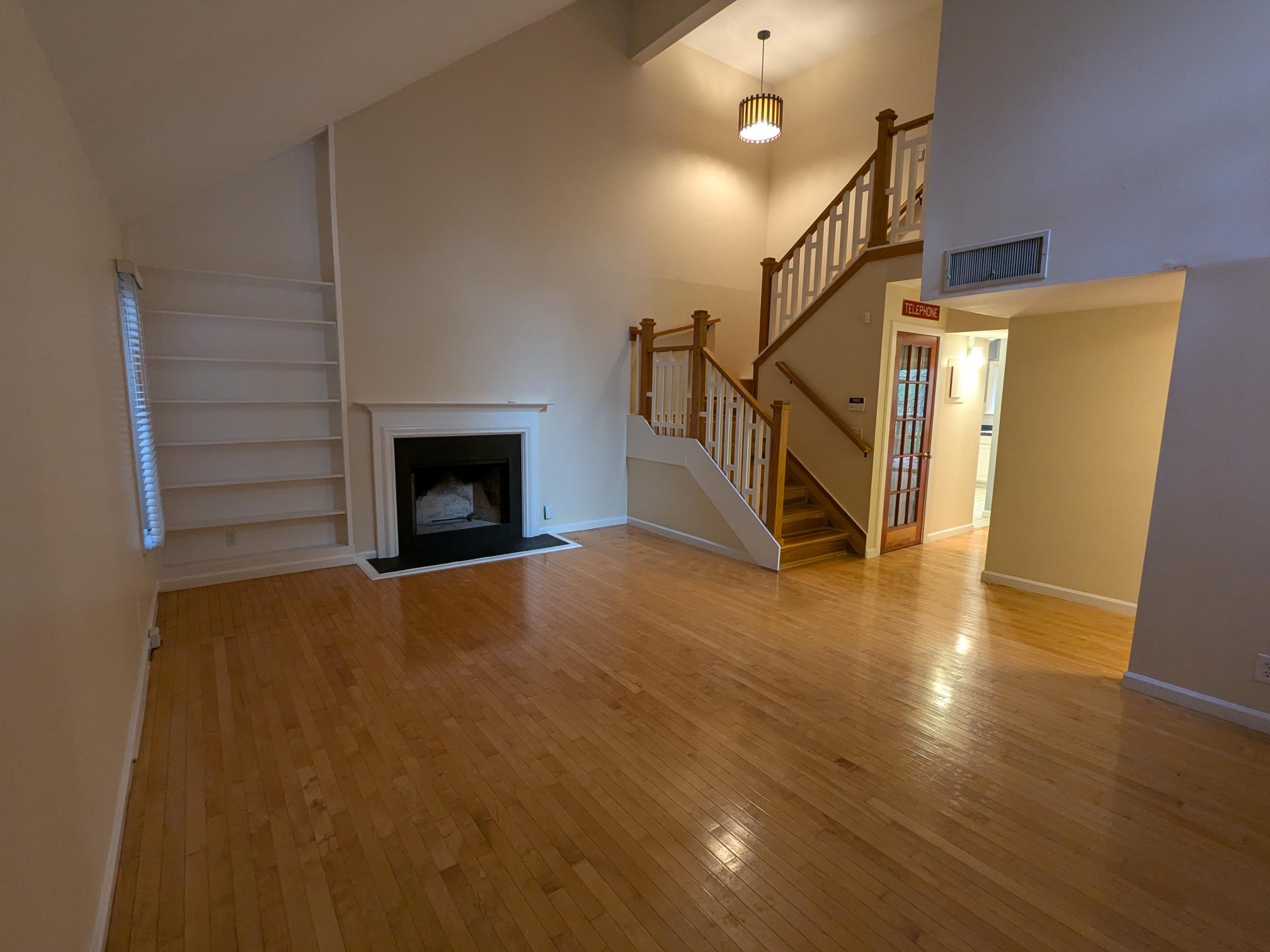 a view of an empty room with wooden floor fireplace and a window