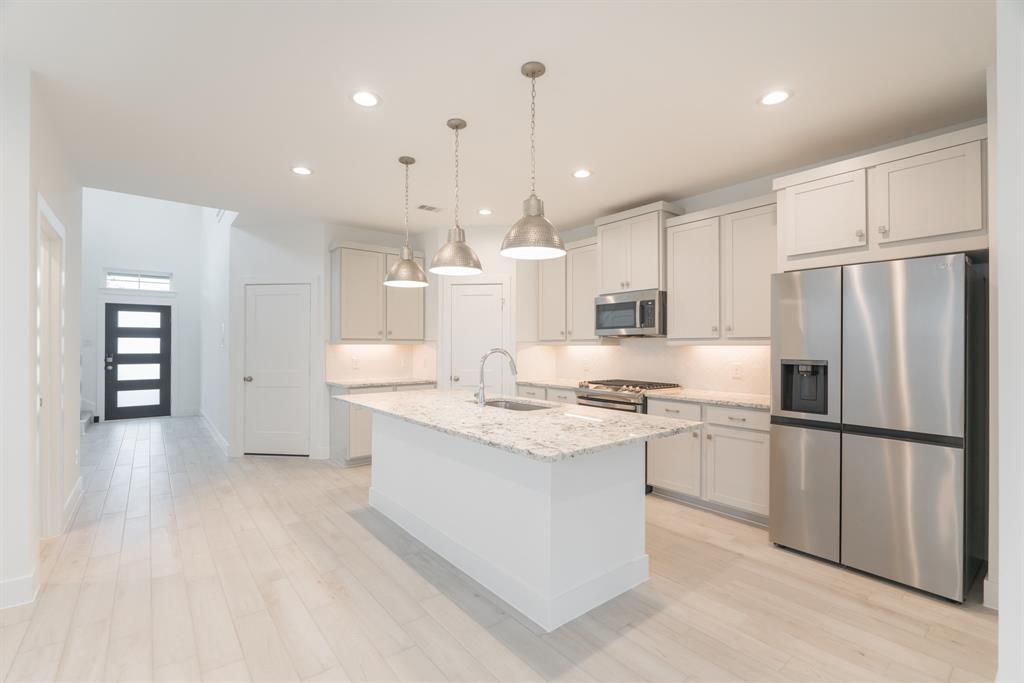 a kitchen with stainless steel appliances kitchen island granite countertop a refrigerator a sink dishwasher a stove and white cabinets with wooden floor