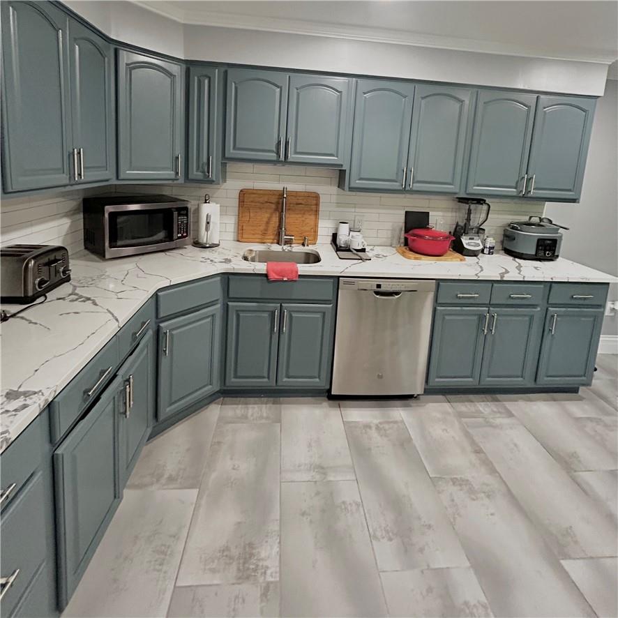 Newly Renovated Kitchen featuring decorative backsplash, ornamental molding, appliances with stainless steel finishes, light stone counters, and sink