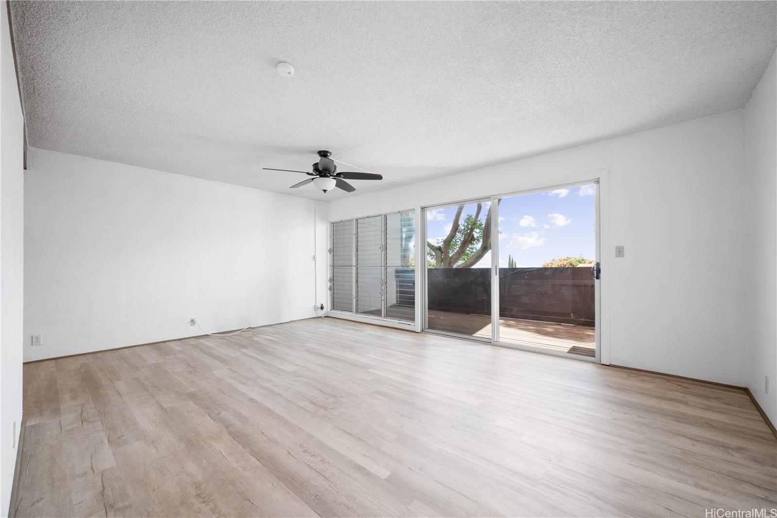 an empty room with wooden floor fan and windows