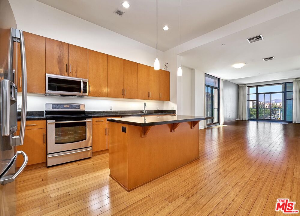 a kitchen with granite countertop wooden floors stainless steel appliances and a counter space