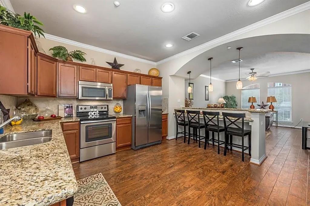 a kitchen with stainless steel appliances kitchen island granite countertop a stove top oven a sink dishwasher a dining table and chairs with wooden floor