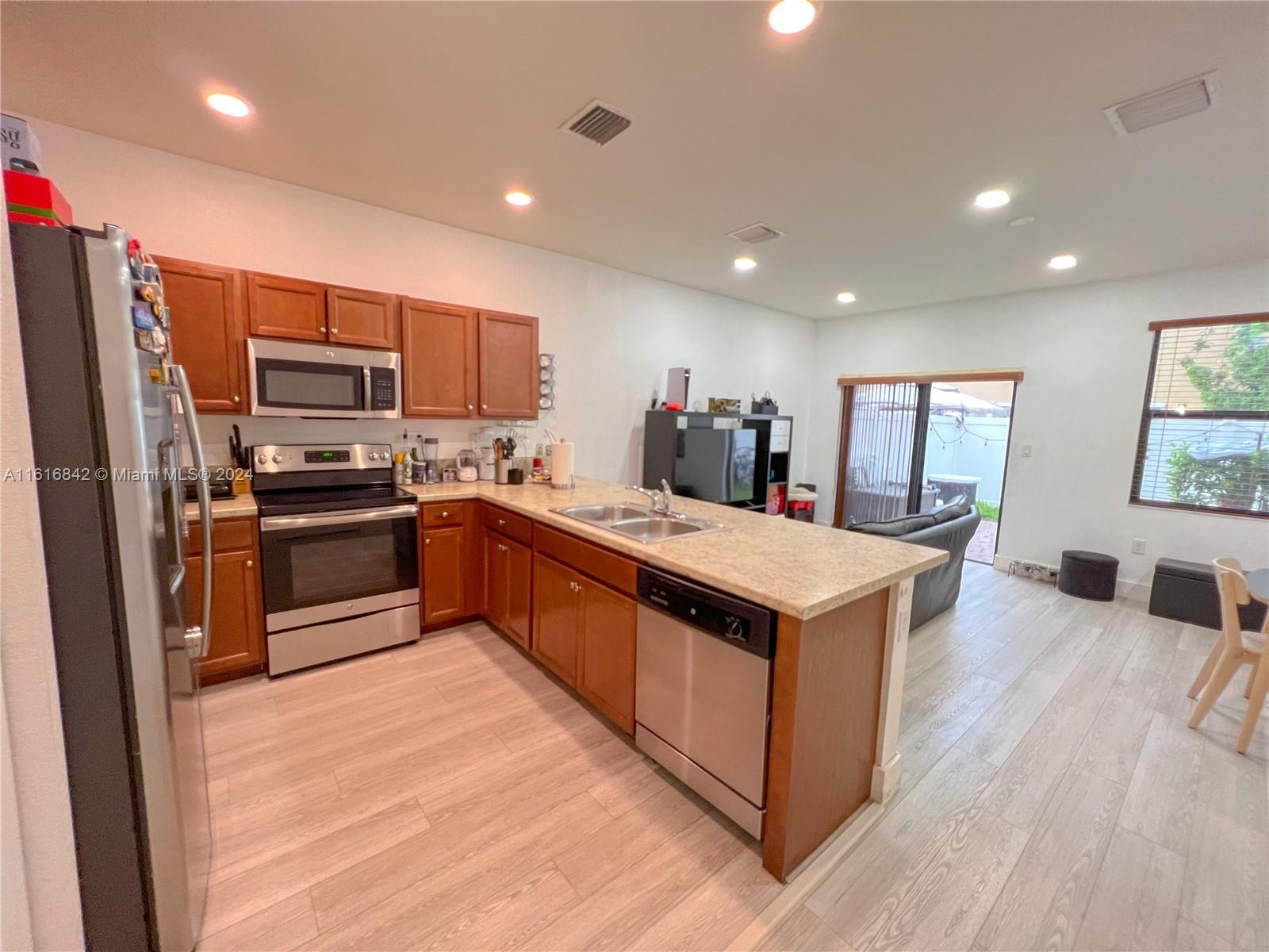 a kitchen with stainless steel appliances granite countertop a stove top oven a sink dishwasher a refrigerator and a refrigerator with wooden floor