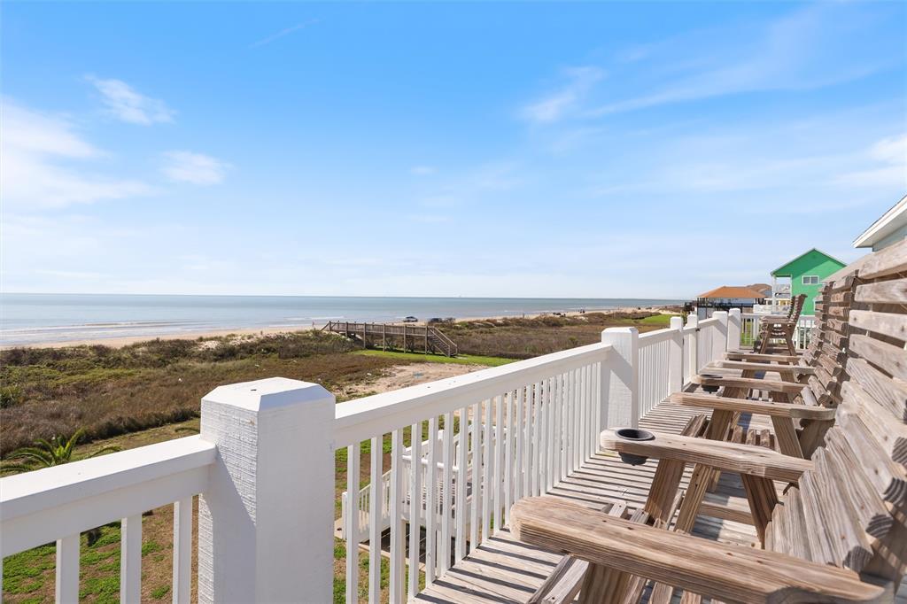 Oceanfront view from your private deck, overlooking a sandy beach, grassy dunes, and a clear sky.