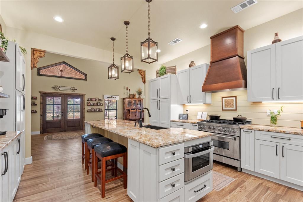 a kitchen with stainless steel appliances granite countertop a stove a sink dishwasher and white cabinets with wooden floor