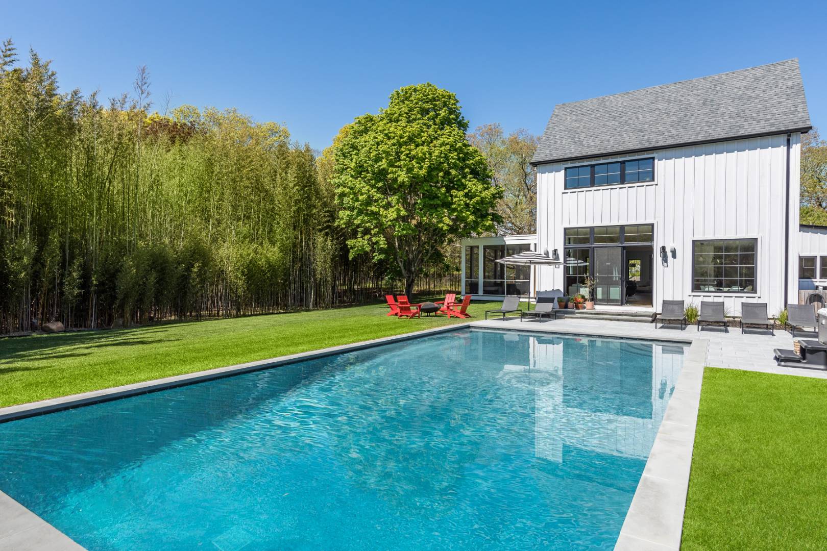 a view of pool with lawn chairs and large trees