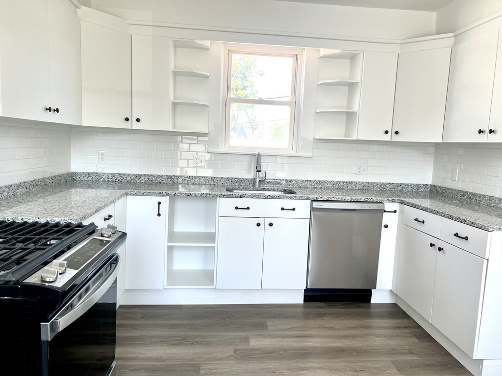 a kitchen with granite countertop a stove a sink and dishwasher with white cabinets