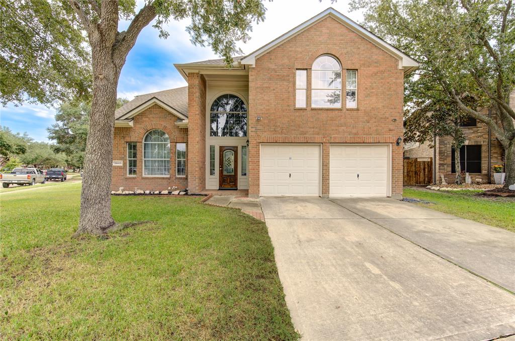 This is a two-story, brick-facade home featuring a double garage and large windows, nestled in a neighborhood with mature trees and a well-maintained lawn.