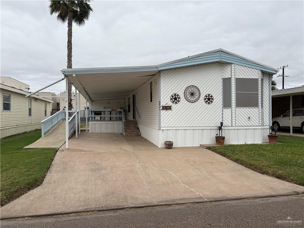 Mobile home featuring a front lawn, covered porch, and a carport