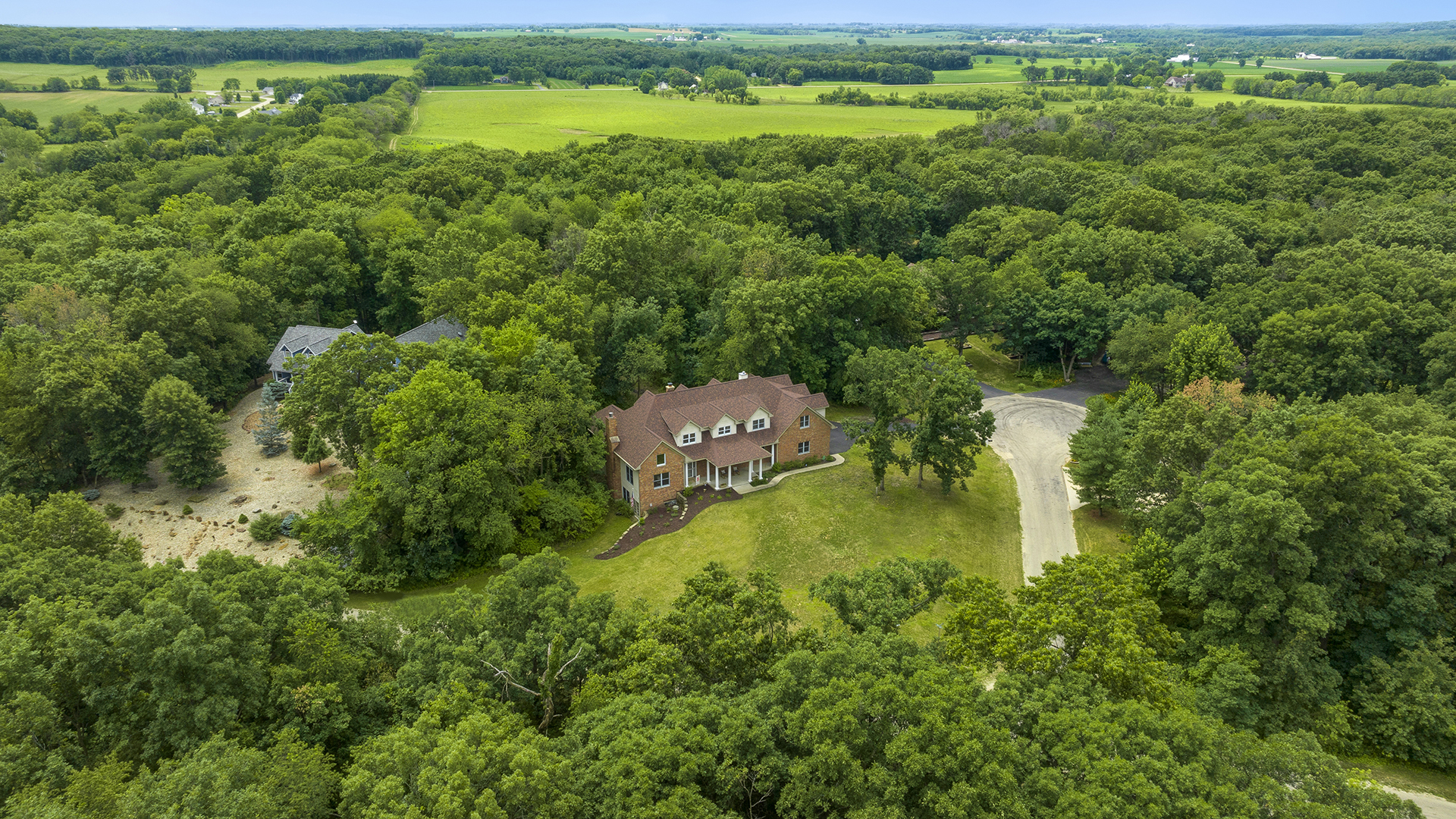 an aerial view of a residential houses with outdoor space and trees all around