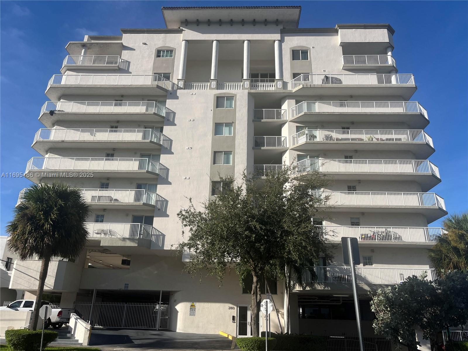 a front view of a multi story residential apartment building with yard and parking