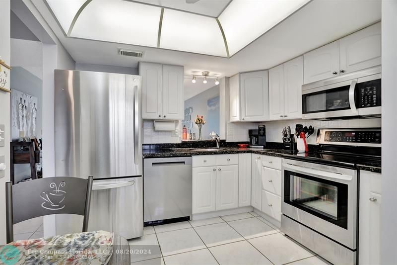 a kitchen with stainless steel appliances granite countertop a refrigerator a stove a sink and white cabinets