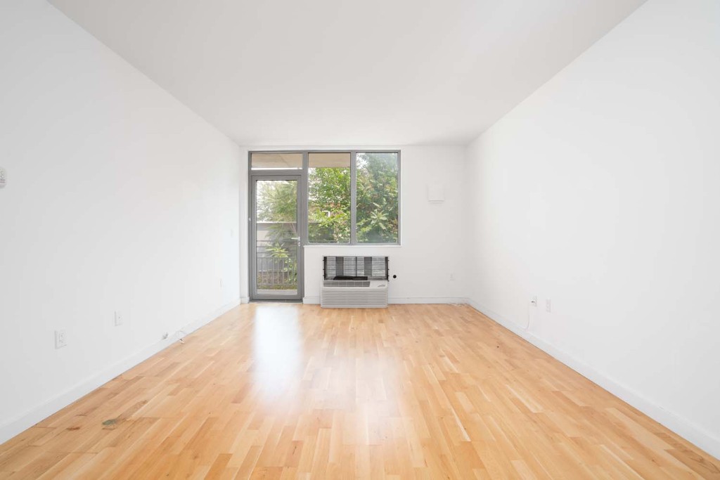 a view of an empty room with a window and wooden floor