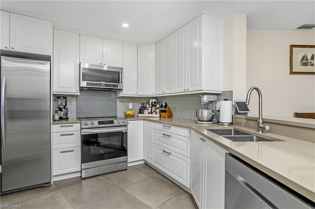 Kitchen featuring stainless steel appliances, sink, backsplash, light tile patterned floors, and white cabinetry