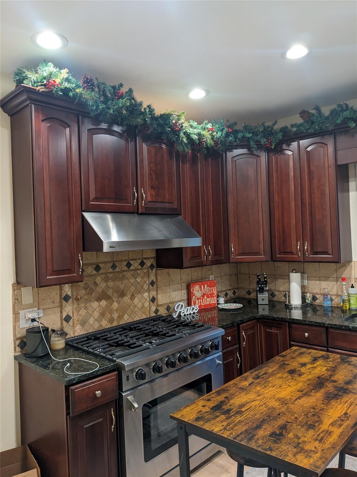 Kitchen featuring dark stone counters, high end stainless steel range, and tasteful backsplash