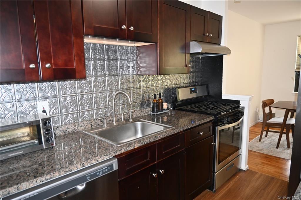 Kitchen with sink, backsplash, extractor fan, stainless steel appliances, and dark hardwood / wood-style flooring