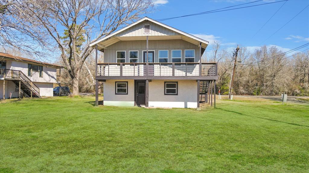 The two-story lake home with balcony, is set on a spacious lawn with mature trees. Featuring a ground-level entry and an external staircase/balcony leading to the upper floor.