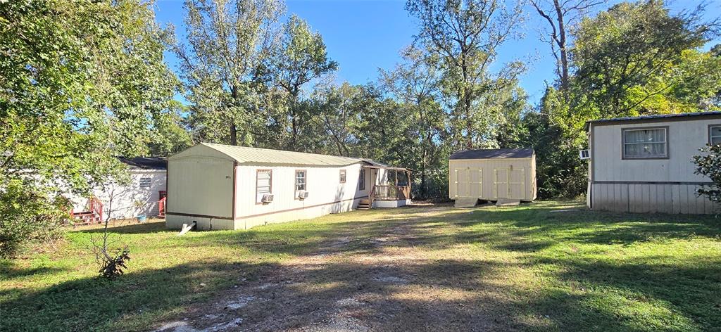 This property features a single-story modular home flanked by trees, with a clear gravel driveway and a structure on that could serve as storage or a workshop. The setting is quiet and peaceful with ample green space.