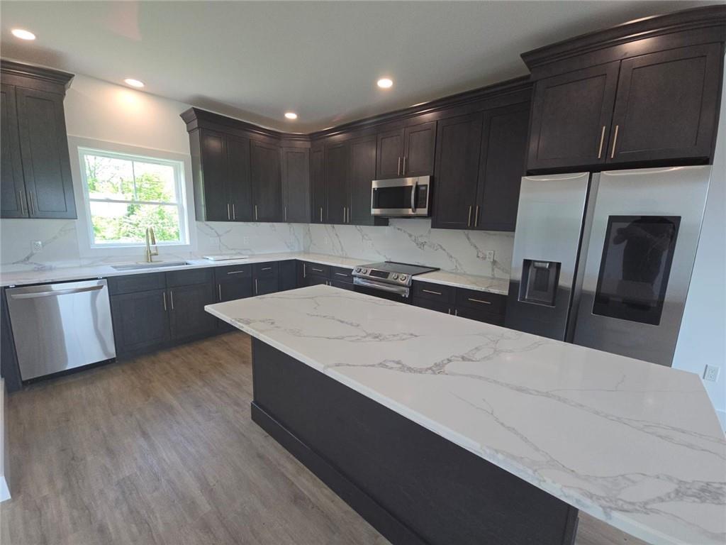 Kitchen featuring tasteful backsplash, stainless steel appliances, sink, light stone counters, and light hardwood / wood-style floors