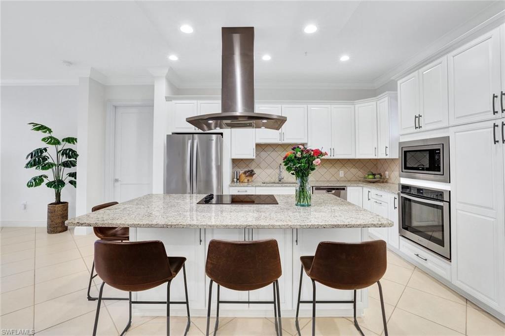 Kitchen with white cabinets, light stone counters, stainless steel appliances, island exhaust hood, and a kitchen island