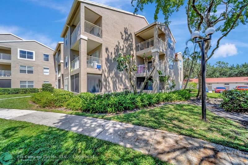 a front view of a multi story residential apartment building with yard and green space