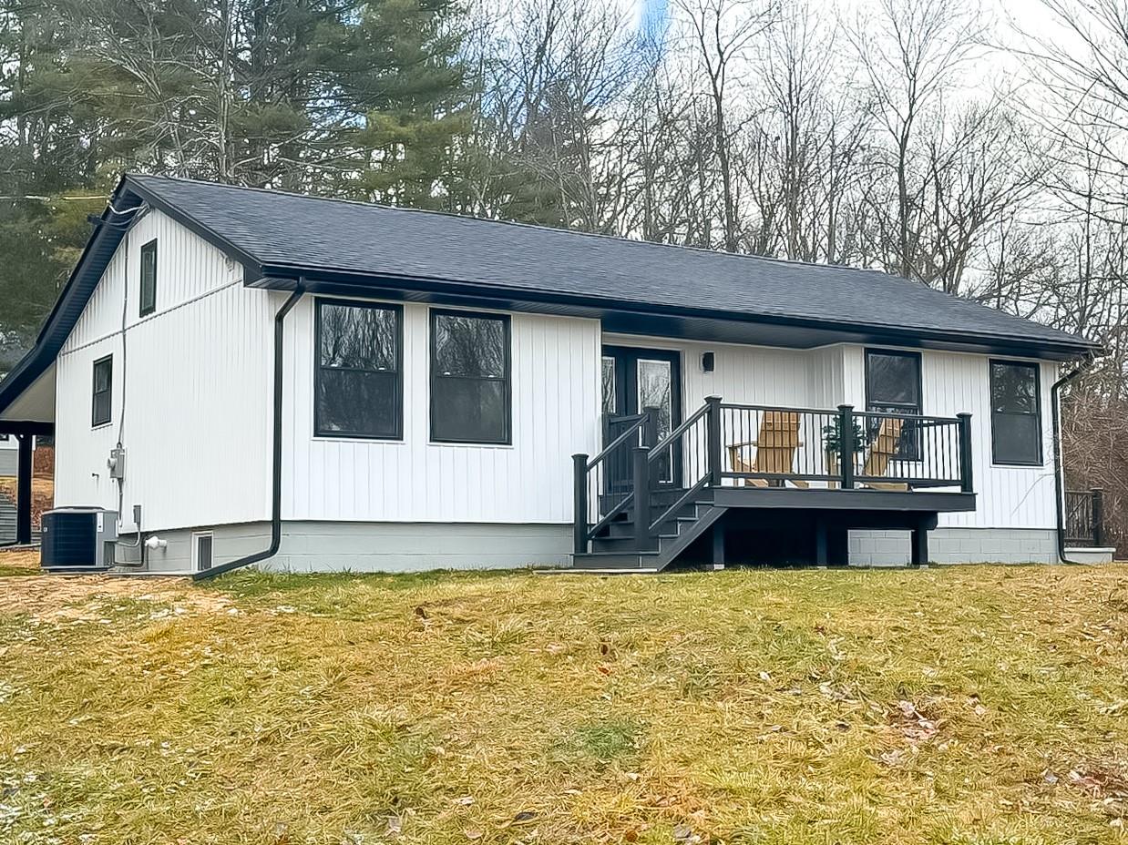 Back of property with a wooden deck, cooling unit, and a lawn